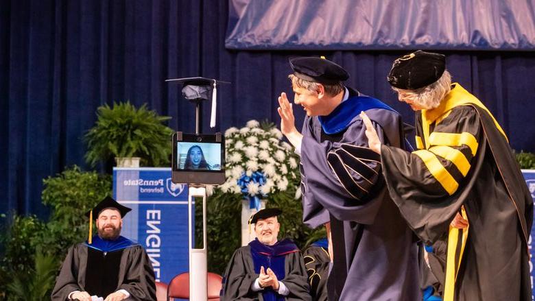 Two Penn State Behrend 教师 members wave to a student whose face is on the monitor of a robot.